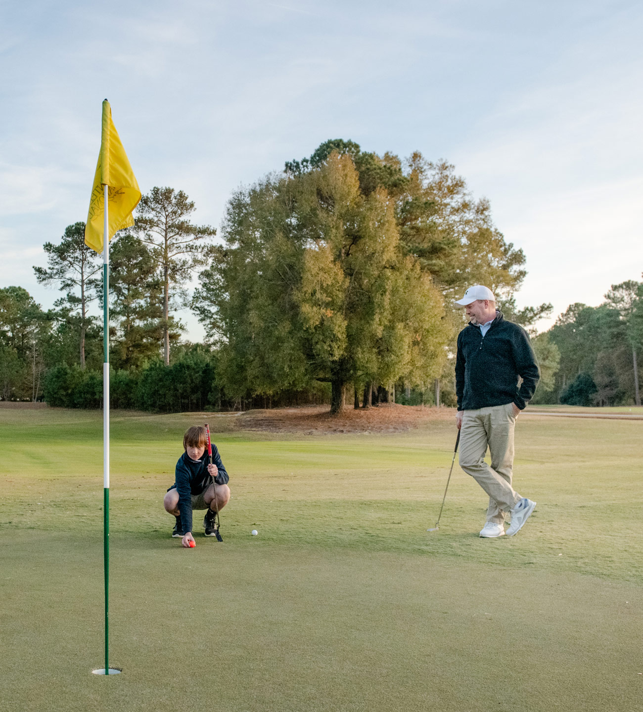 Father watching while son lines up a putt on the golf green