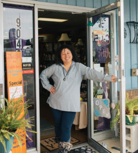 woman standing with open door to antiques shop, welcoming with a smile